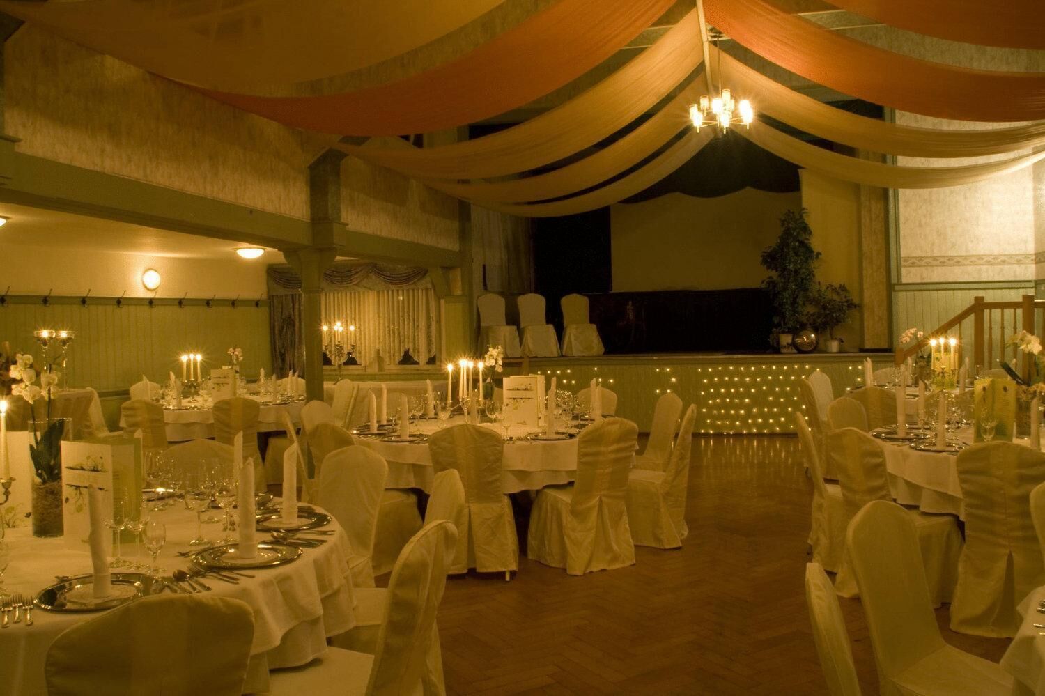 Un salón de banquetes con mesas redondas dispuestas para un evento formal, con candelabros y centros de mesa con velas.