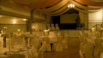 Un salón de banquetes con mesas redondas dispuestas para un evento formal, con candelabros y centros de mesa con velas.