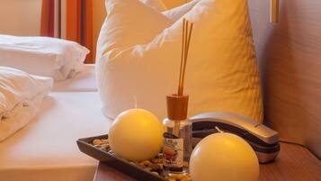 A hotel room with a neatly made bed, a bedside lamp, a remote control, and a tray with candles and a bottle.
