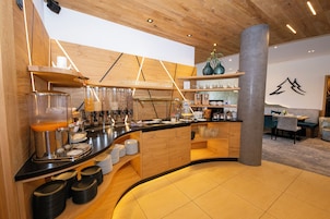 Un café moderno con mostrador de madera, estanterías con cristalería y una zona de estar con mesas y sillas.