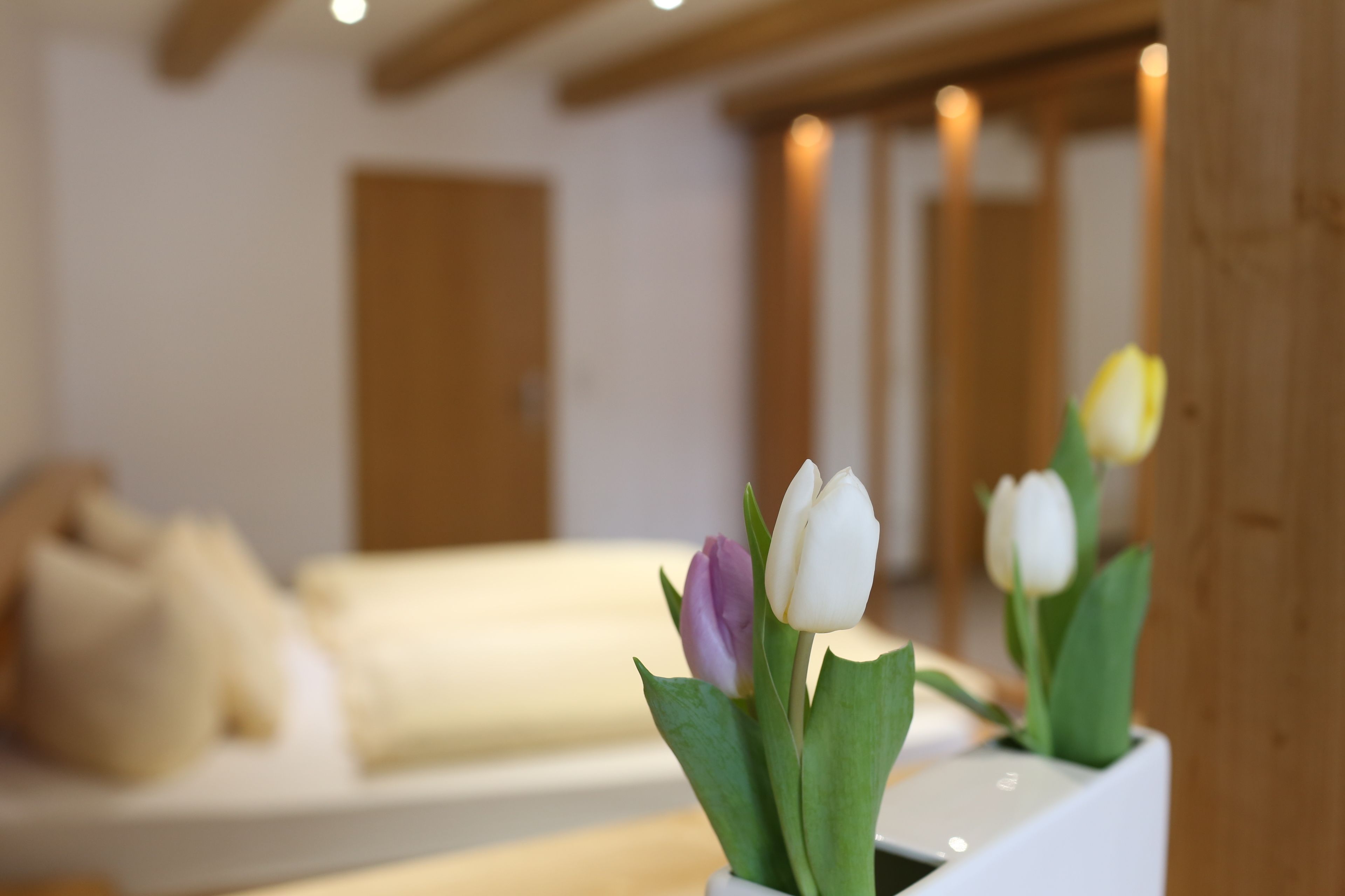 A room with a bed, a wooden headboard, and a vase with tulips.