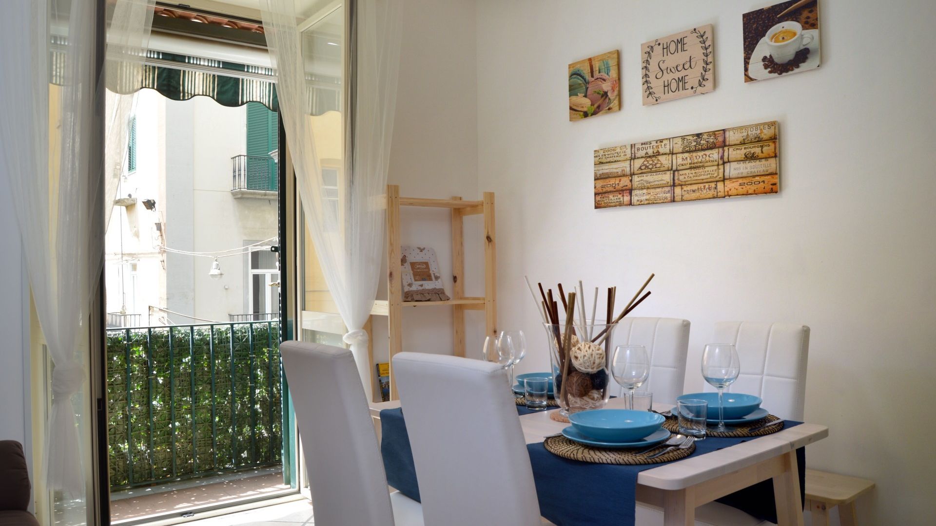Ein Essbereich mit einem Tisch für zwei Personen, einem Holzregal und Blick auf den Außenbalkon.