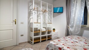 A bedroom with a bed, a wardrobe with hanging space, a small bedside table, and a television on the wall.