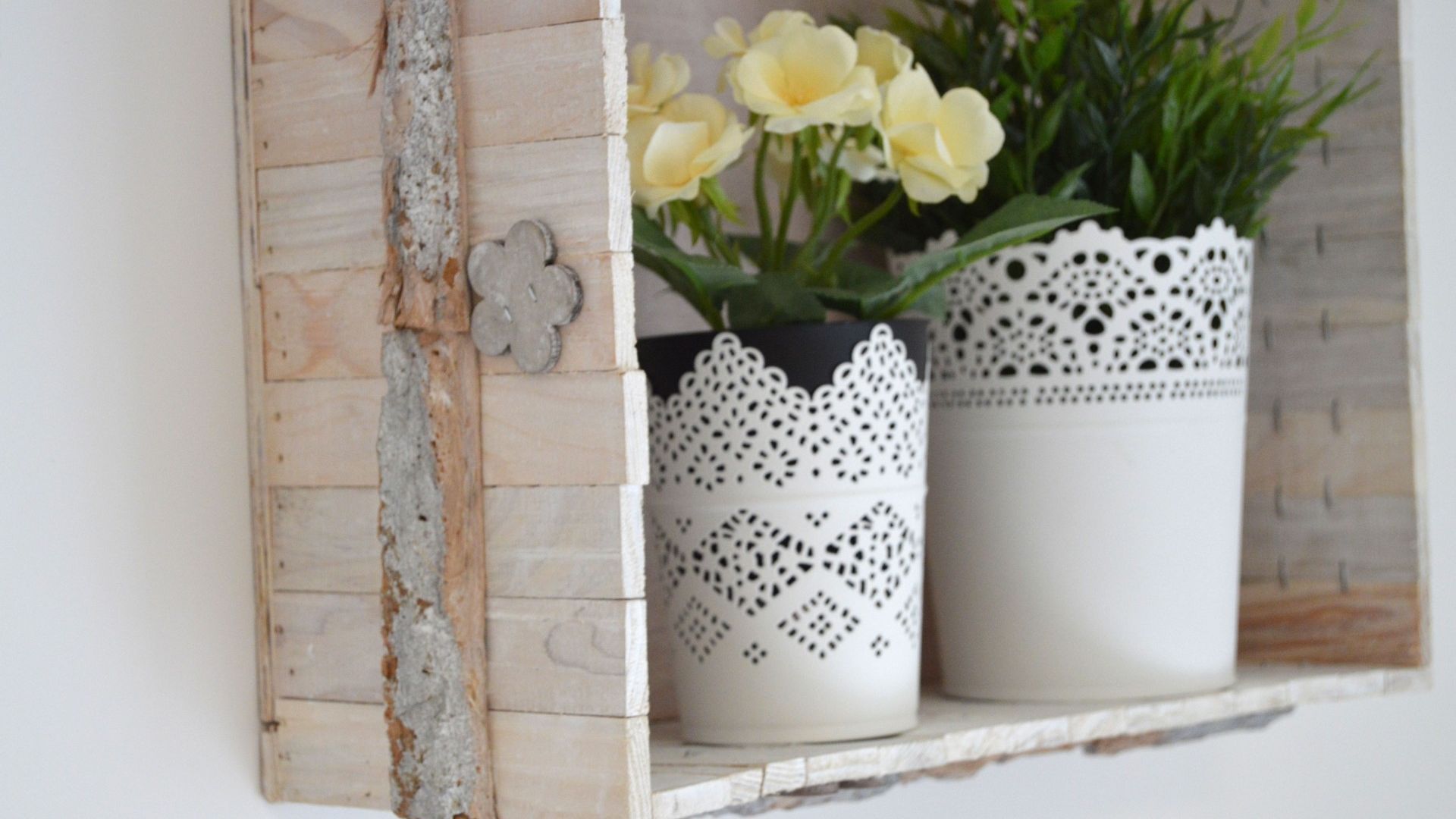 Two white ceramic vases with intricate cut-out patterns on a shelf.
