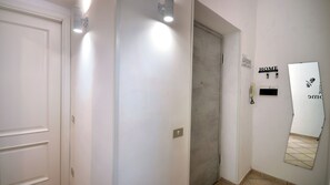 Un couloir avec une porte, un luminaire fixé au mur, une pancarte de bienvenue et une clé accrochée au mur.