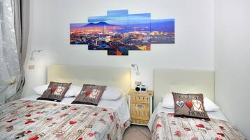 Ein Hotelzimmer mit zwei Betten, jeweils mit einem Bettbezug und Kissen mit Herzmuster. Zwischen den Betten befindet sich ein Nachttisch mit Radio und Lampe. Darüber hängt ein großes Stadtbild.