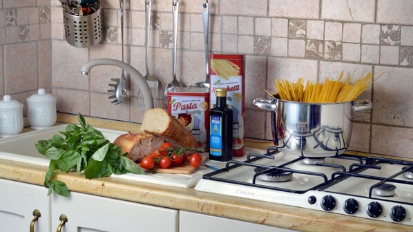 A kitchen with a gas stove, a box of pasta, a bottle of olive oil, and fresh tomatoes.