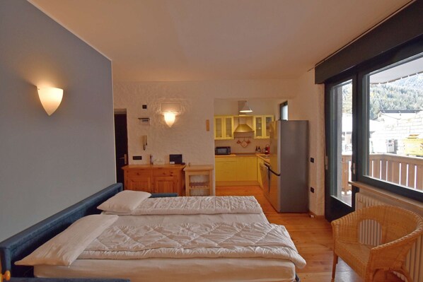 A bedroom with two beds, a kitchen in the background, and a view through a large window. - SISSI APARTMENT (Madonna di Campiglio)
