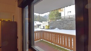 Vista desde una ventana a un balcón con baranda de madera, suelo cubierto de nieve y una montaña al fondo.