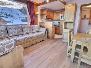 A cozy cabin interior with a wooden sofa, a dining table, and a kitchen area.