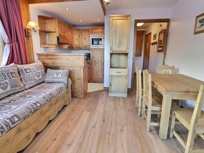 Interior acogedor de una cabaña con sofá de madera, mesa de comedor y zona de cocina.