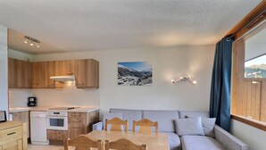 A compact kitchen with wooden cabinets, a dining table with chairs, a sofa, and a painting of a snowy landscape. - Cozy Apartment in Méribel, 4 pers, Pets allowed (Méribel)