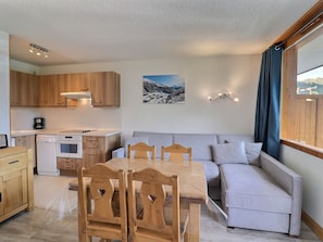 A compact kitchen with wooden cabinets, a dining table with chairs, a sofa, and a painting of a snowy landscape. - Cozy Apartment in Méribel, 4 pers, Pets allowed (Méribel)