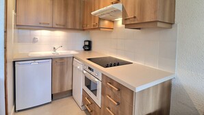 A compact kitchen with wooden cabinets, a built-in oven, a dishwasher, and a stovetop. - Cozy Apartment in Méribel, 4 pers, Pets allowed (Méribel)