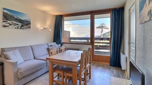 A cozy room with a wooden dining table, a sofa, and a large window offering a view of a mountain landscape. - Cozy Apartment in Méribel, 4 pers, Pets allowed (Méribel)