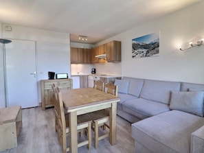 Um espaço de estar compacto com cozinha compacta, uma mesa de jantar com cadeiras, um sofá e um quadro pendurado na parede.