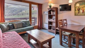 A cozy room with a sofa, a wooden table, a bookshelf, and a TV mounted on the wall.
