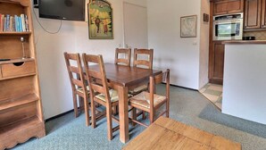 A dining area with a wooden table and chairs, a television mounted on the wall, and a kitchen with wooden cabinets and appliances.