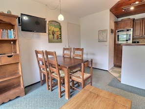 A dining area with a wooden table and chairs, a television mounted on the wall, and a kitchen with wooden cabinets and appliances. - Comfortable apartment, south balcony, 4 ppl, double bed (Méribel)