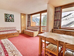 A cozy room with a wooden bench, a table, and large windows offering a mountain view.