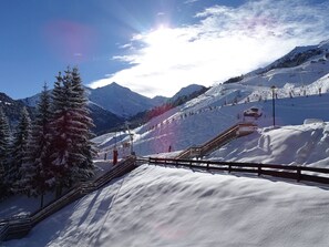 Un paisaje montañoso cubierto de nieve, con un telesilla, barandas de madera y árboles nevados.