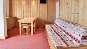 Une pièce aux murs en bois, avec une table en bois et des chaises, un canapé, un téléviseur fixé au mur et un petit meuble.