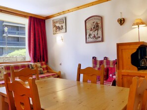 A dining area with a wooden table and chairs, a bench with a plaid blanket, and two wall-mounted pictures depicting historical scenes.