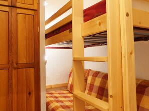 A bunk bed with a checkered blanket, wooden headboard, and a red pillow.