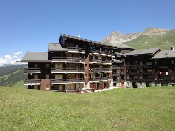A multi-story hotel with balconies, set against a mountainous backdrop.