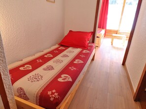 A small, single-bed room with a red and white patterned bedspread, wooden headboard, and a red pillow.