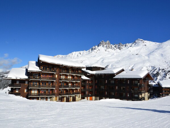 A multi-story lodge with balconies, set against a snowy mountain backdrop.