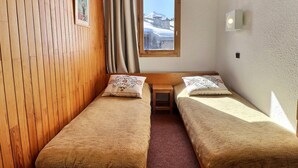 A small room with two single beds, a wooden wall, a window with a view of a mountain, and a small table. - Ski-in studio, pets allowed, sleeps 4 (Méribel)