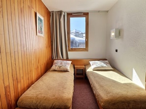A small room with two single beds, a wooden wall, a window with a view of a mountain, and a small table. - Ski-in studio, pets allowed, sleeps 4 (Méribel)