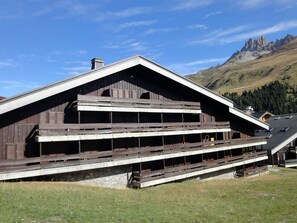 A wooden chalet with a sloped roof and multiple balconies, set against a mountainous backdrop.