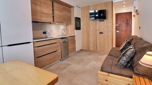 A compact kitchen with wooden cabinets, a built-in oven, and a TV mounted on the wall.