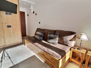 A cozy room with a wooden sofa, two pillows, a small wooden side table with a lamp, and a wooden cabinet.