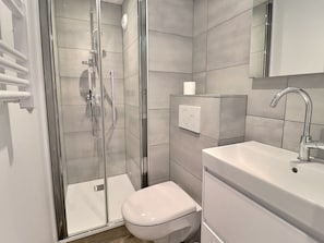 A modern bathroom with a glass-enclosed shower, a toilet, and a sink with a mirror above.