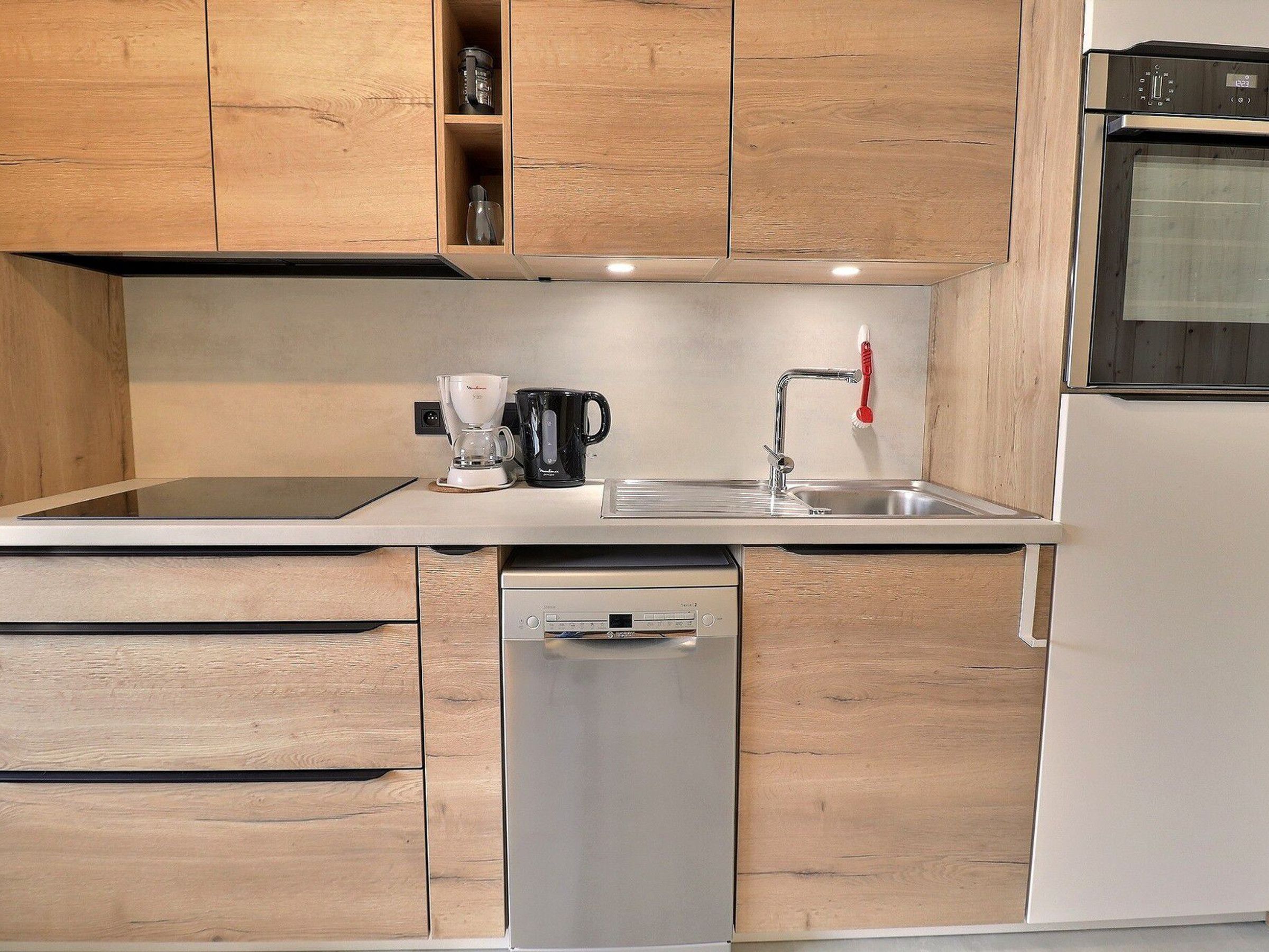 A kitchen with wooden cabinets, a dishwasher, a coffee maker, and a refrigerator.