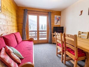 A wooden cabin interior with a red sofa, a wooden dining table with chairs, a television, and a view of a snowy landscape through the windows. - Cozy 2-room apt for 4 on the slopes in Méribel (Méribel)
