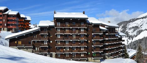 Un hotel de varios pisos con balcones y una pista de esquí al fondo.