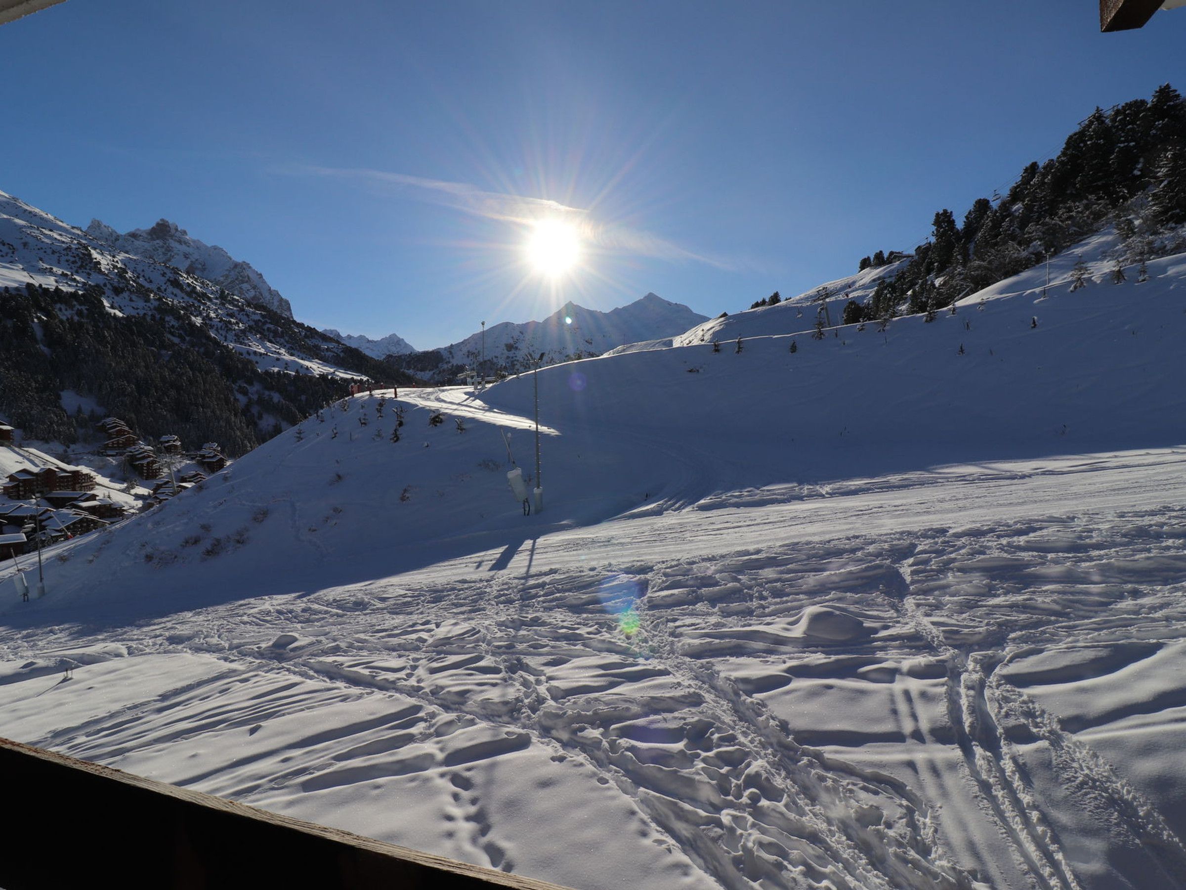 A snowy mountain slope with ski tracks, a ski lift, and a clear sky.