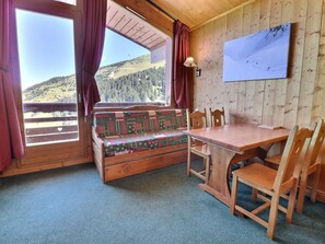 A wooden cabin with a bench, table, chairs, and a view of a mountainous landscape.