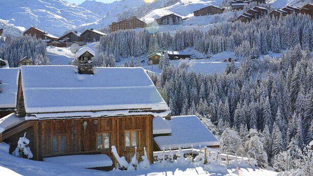 Un village de montagne enneigé, avec des chalets en bois, un télésiège et une vue dégagée sur les montagnes environnantes.
