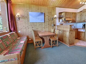 A cozy cabin interior with a wooden dining table, chairs, a sofa, and a kitchen area.