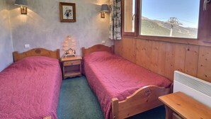 A room with two wooden beds, a nightstand, a small table, a window with a view of a mountain, and a wall-mounted lamp. - Charming 2-Room, 4 People, Pets Allowed with Wi-Fi (Méribel)