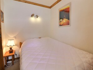 Une chambre à coucher avec un lit, une lampe de chevet, un luminaire fixé au mur et un tableau encadré.