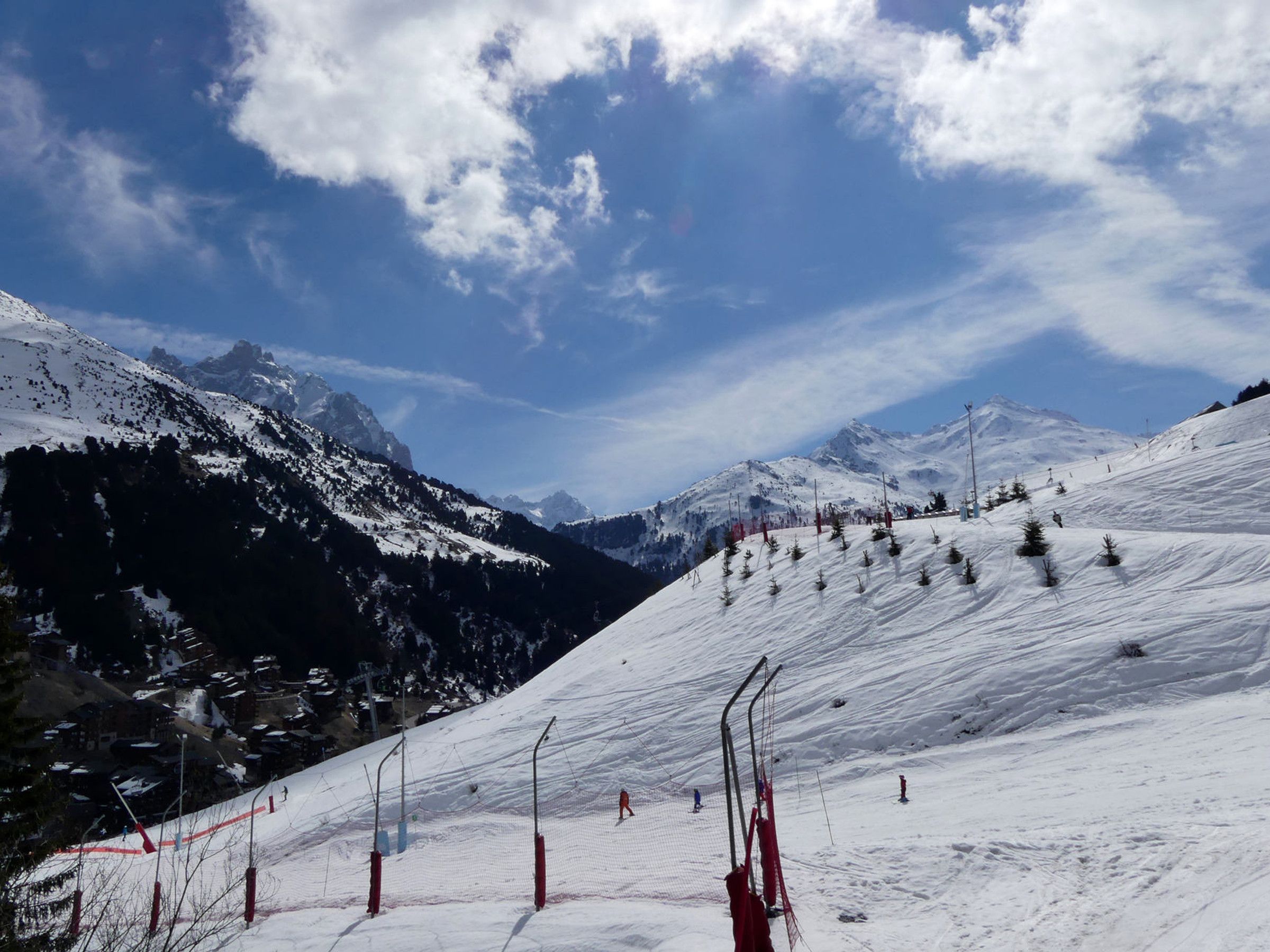 A snow-covered ski slope with a clear sky and mountains in the background.
