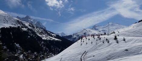 A snow-covered ski slope with a clear sky and mountains in the background.