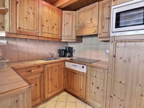 Una cocina con armarios de madera, un lavamanos de acero inoxidable, una cafetera y un microondas.