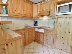 A kitchen with wooden cabinets, a microwave, a dishwasher, and a coffee maker. - Charming 2-Room Apartment Méribel - 5 Pers, South Balcony, Wi-Fi (Méribel)